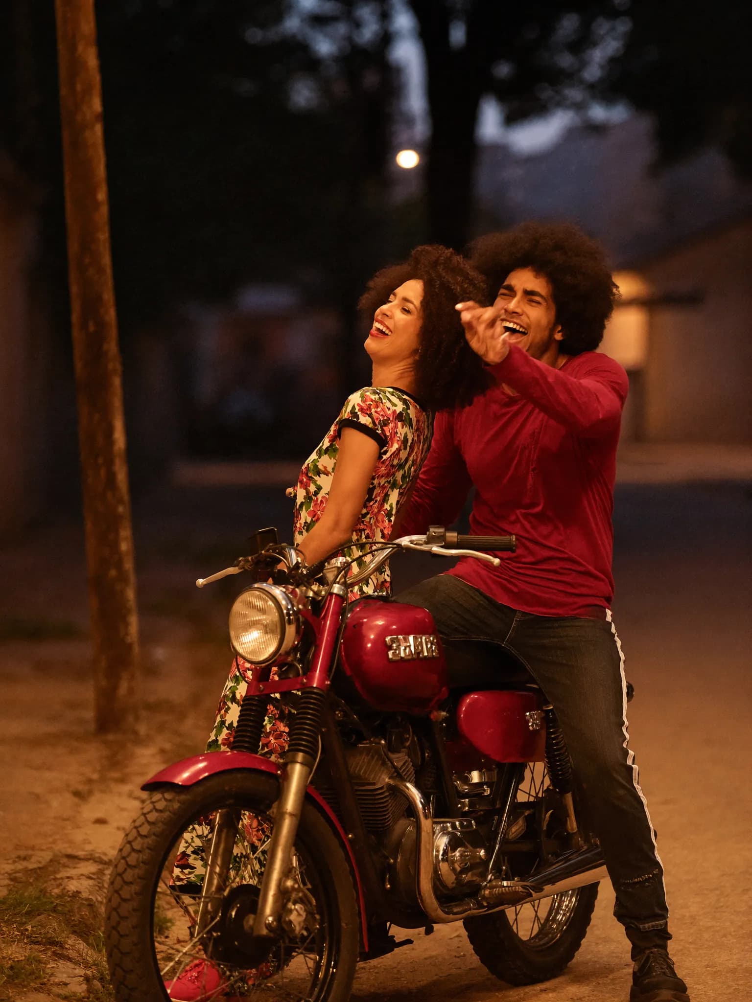Casal afrodescendente sorrindo encostado em moto antiga