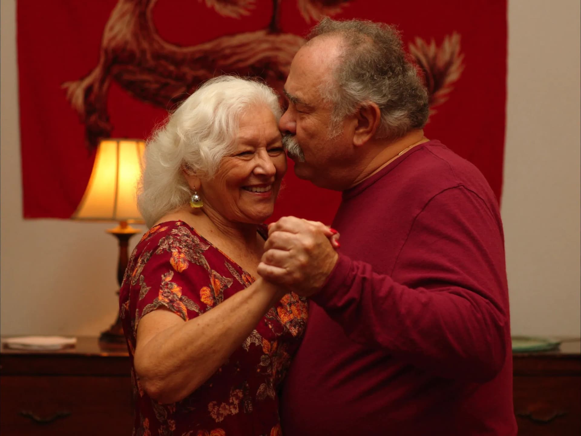 Casal idoso brasileiro dançando lentamente na sala com luz dourada
